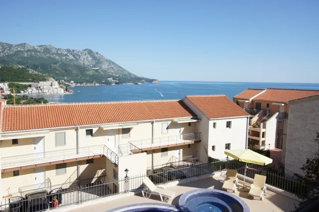 Pogled na more i planine iz apartmana u Bečićima, Crna Gora: bazen sa ležaljkama i stambeni kompleks sa krovom od crepa.