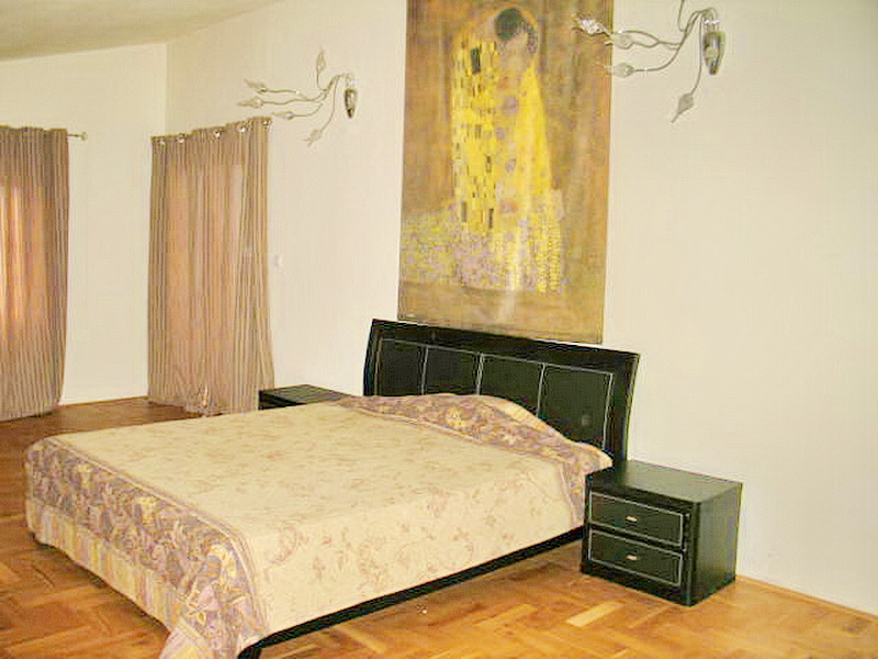 Bedroom with a double bed and a painting in a house in Dobri Vody, Montenegro: parquet floor and light walls.