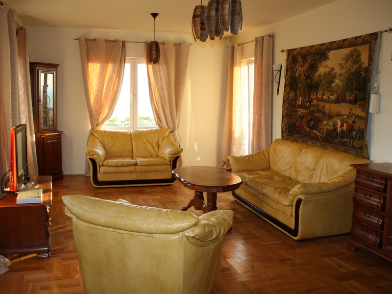 Living room with leather furniture and parquet flooring in a house in Dobri Vody, Montenegro. Cozy interior with a tapestry and a view from the windows.