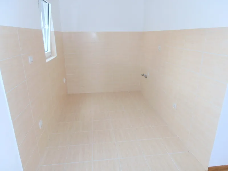 Prazna kuhinja sa bež pločicama i izvedenim instalacijama u novom stanu u Budvi, Crna Gora.