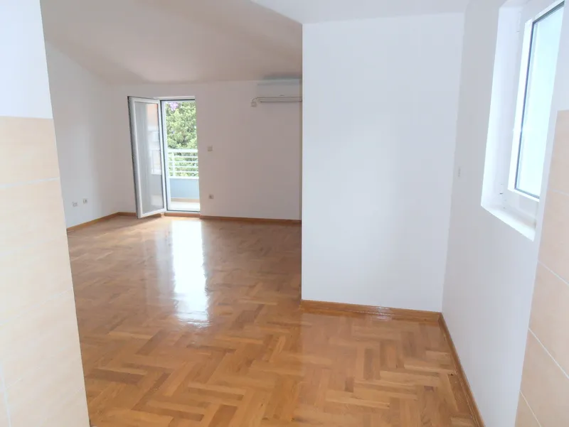 Svetla dnevna soba sa parketom, izlazom na balkon i klima-uređajem u stanu u Budvi, Crna Gora.
