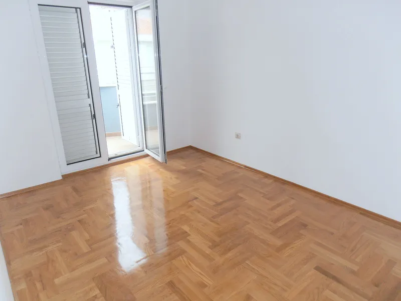 Svetla spavaća soba sa parketnim podom i izlazom na balkon u stanu u Budvi, Crna Gora.
