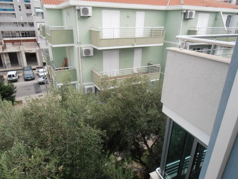 Pogled s balkona na susednu stambenu zgradu i masline u Budvi, Crna Gora. Stan sa terasom i klima-uređajima.