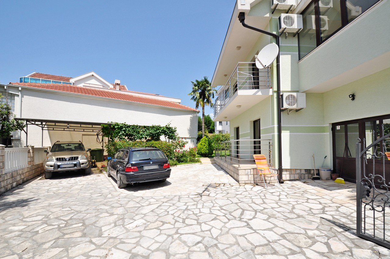 Innenhof des Hauses in Tivat, Montenegro: Parkplatz für zwei Autos, gepflasterte Fläche, Balkon und Grünfläche.