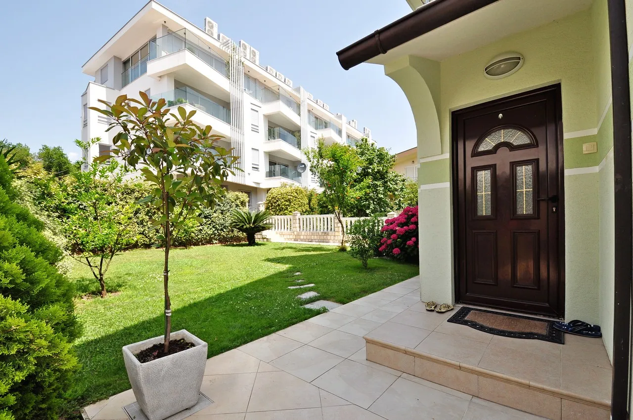 Saksı bitkisi, giriş kapısı ve arka planda apartman bulunan yeşil avlu.
