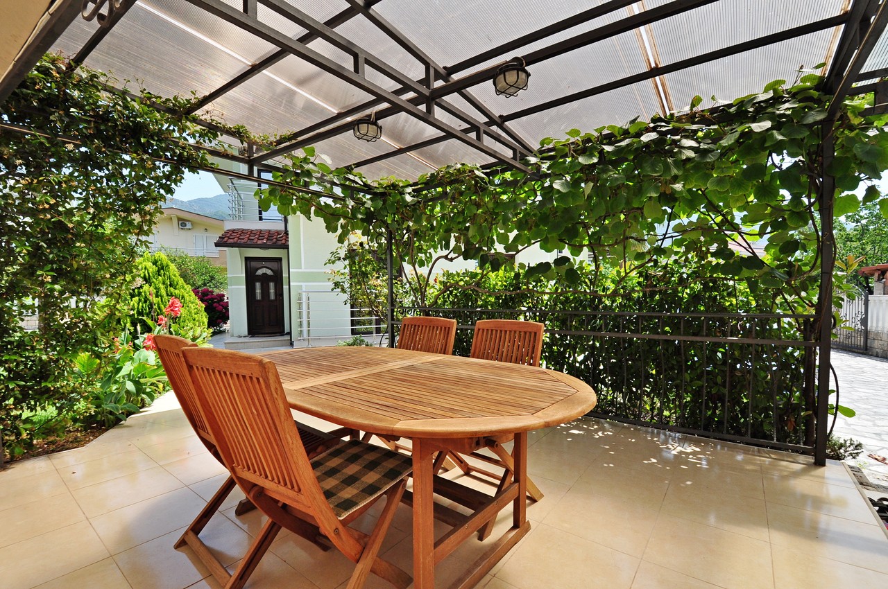 Gemütliche Terrasse mit Holzmöbeln und Überdachung in einem Privathaus in Tivat, Montenegro, umgeben von einem grünen Garten.