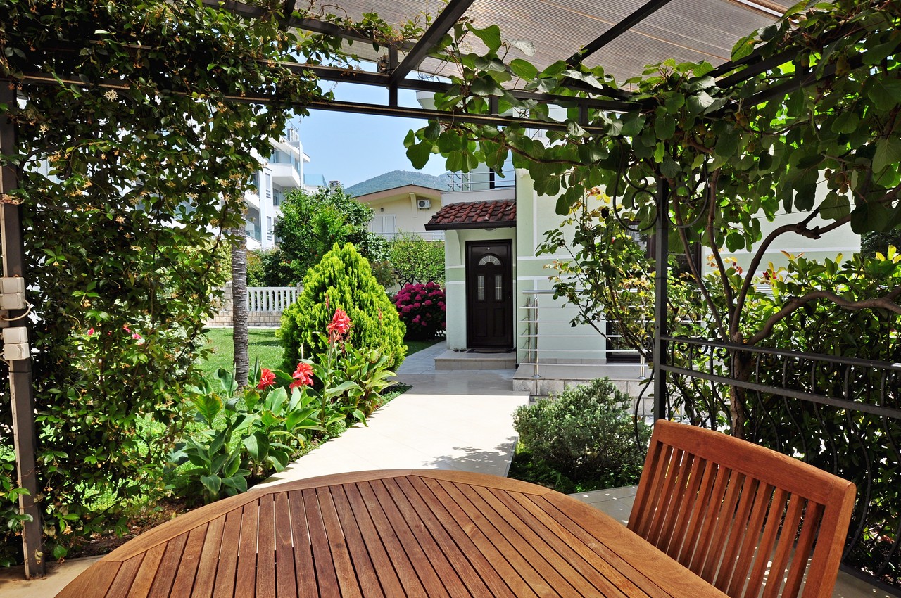 Gemütliche Terrasse mit Holztisch und grünem Garten am Haus in Tivat, Montenegro, Blick auf das gepflegte Grundstück.