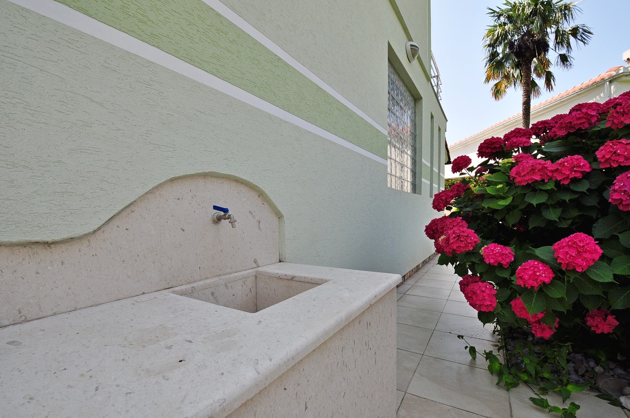 Steinwaschbecken im Hof eines Hauses in Tivat, Montenegro, neben blühenden Hortensien und einer Palme auf dem Grundstück.
