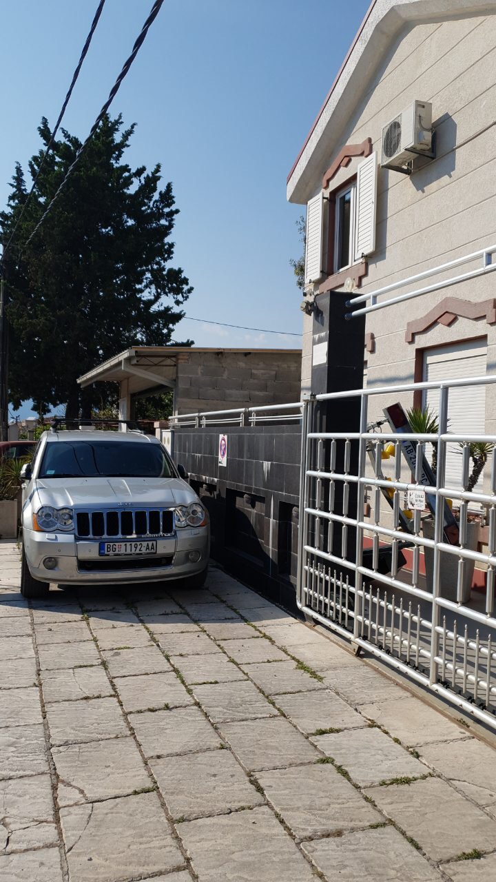 Fasada kuće u Tivtu, Crna Gora: privatni parking sa metalnim kapijama i kamenom popločana površina.