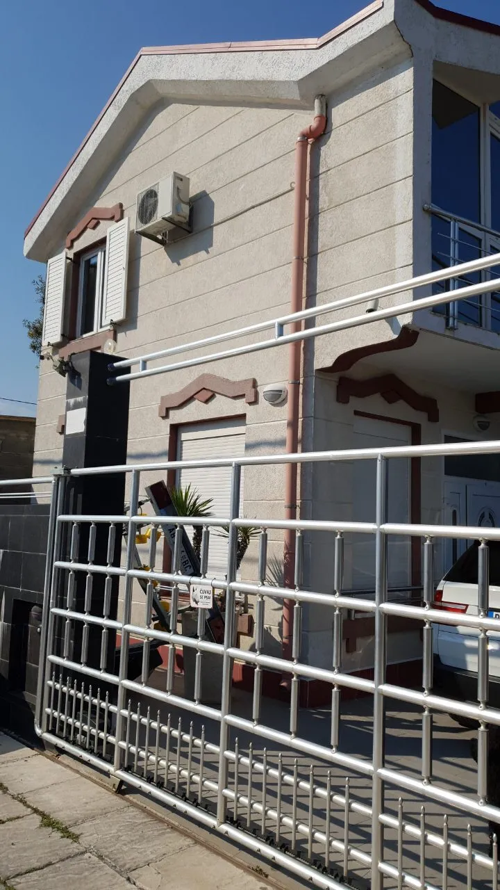 Fassade eines hellen Hauses mit Metallzaun und Tor im Vordergrund.