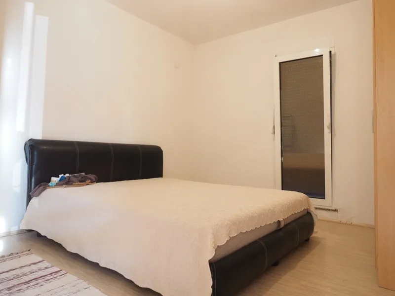 Svetla spavaća soba sa bračnim krevetom u kući u gradu Bar, Crna Gora: savremena završna obrada i izlaz na balkon.