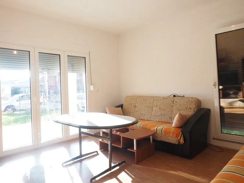Svetla dnevna soba sa sofom i trpezarijskim stolom u kući, grad Bar, Crna Gora. Panoramski prozori sa izlazom na ulicu.