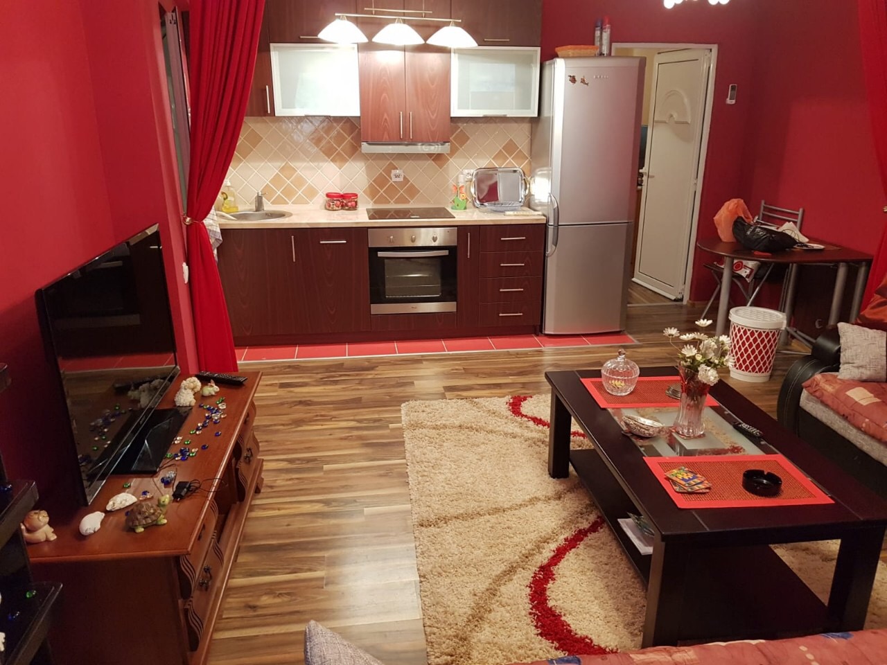 Innenraum des Wohnzimmers mit Küche in einer Wohnung in Budva, Montenegro: dunkle Möbel, rote Wände und ein gemütlicher Teppich.