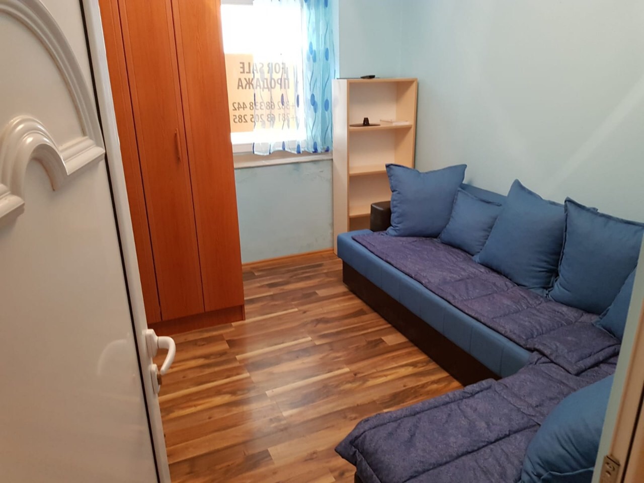 Wohnzimmer in einer Wohnung in Budva, Montenegro: blaues Ecksofa, Holzschrank, Regal und Laminatboden.