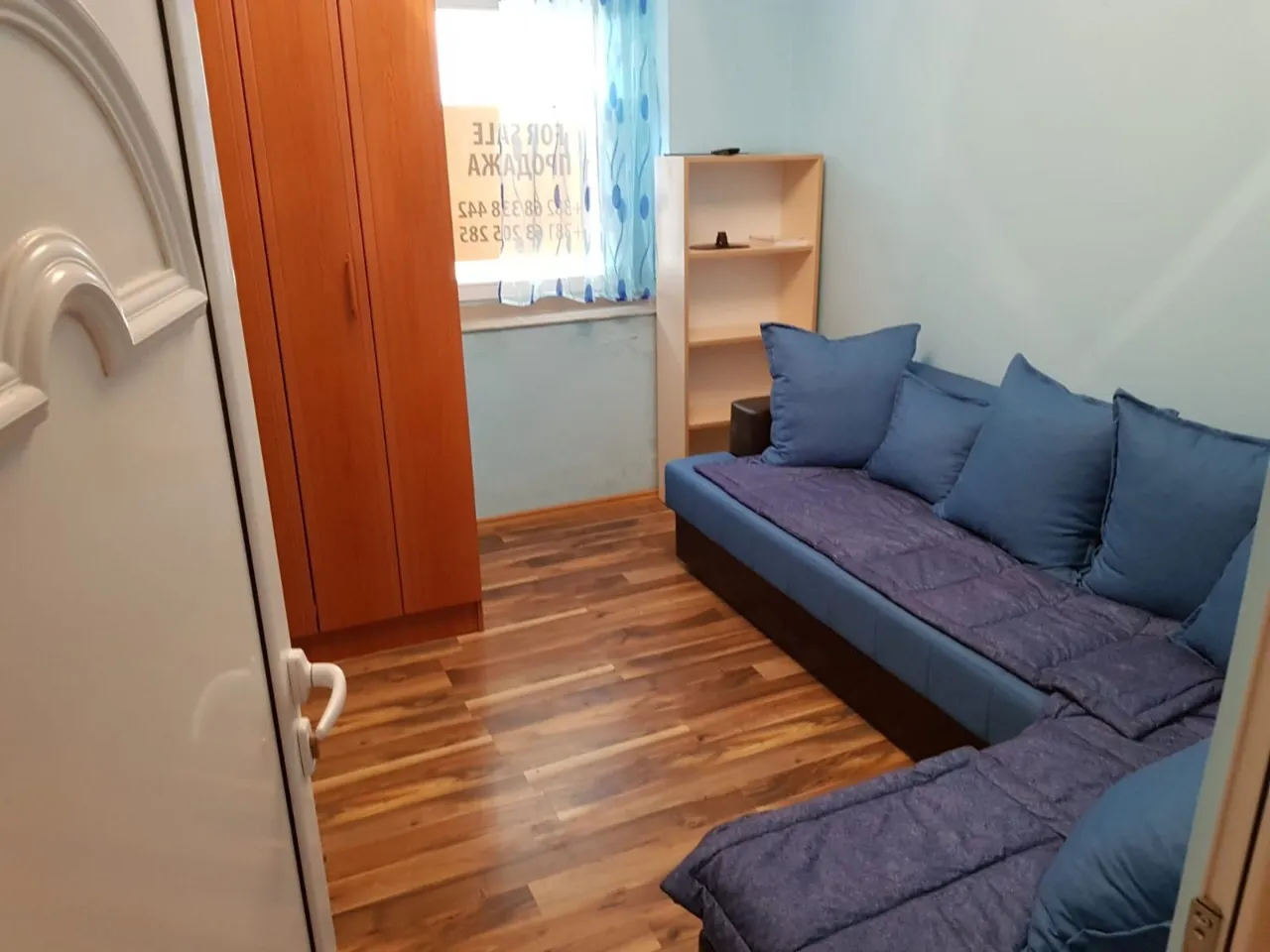 Karadağ, Budva’daki dairede oturma odası: mavi köşe kanepe, ahşap dolap, raf ünitesi ve zeminde laminat.