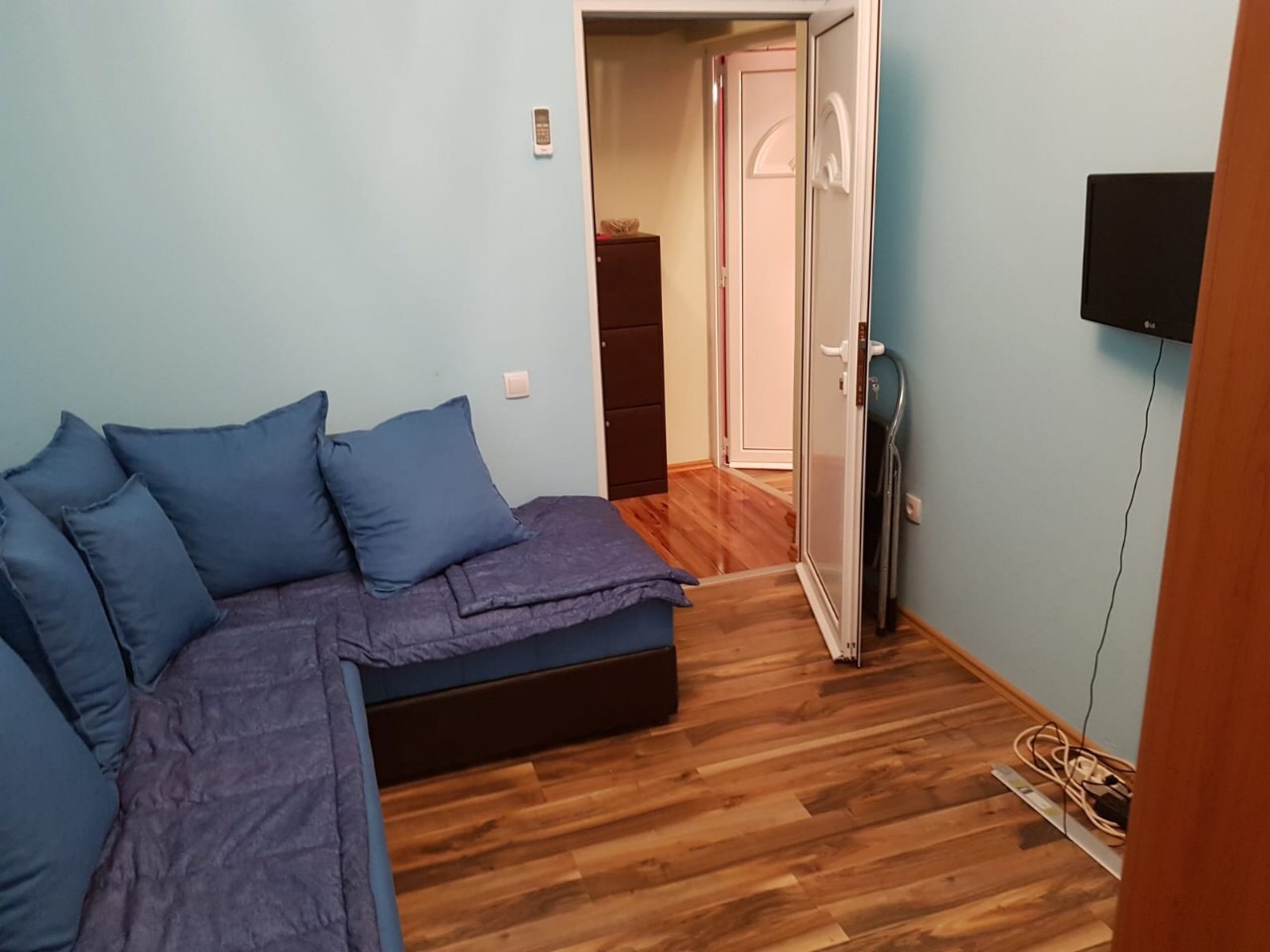 Wohnzimmer mit blauem Ecksofa, Laminatboden und Fernseher in einer zum Verkauf stehenden Wohnung in Budva, Montenegro.