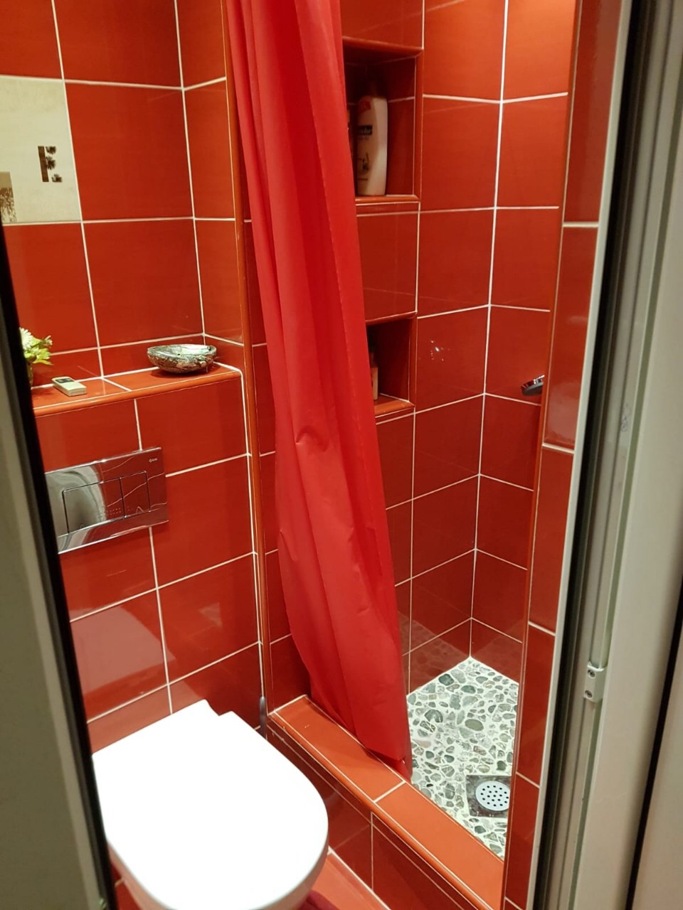 Badezimmer mit roten Fliesen, Duschkabine und Vorwandinstallation in einer Wohnung, Stadt Budva, Montenegro.