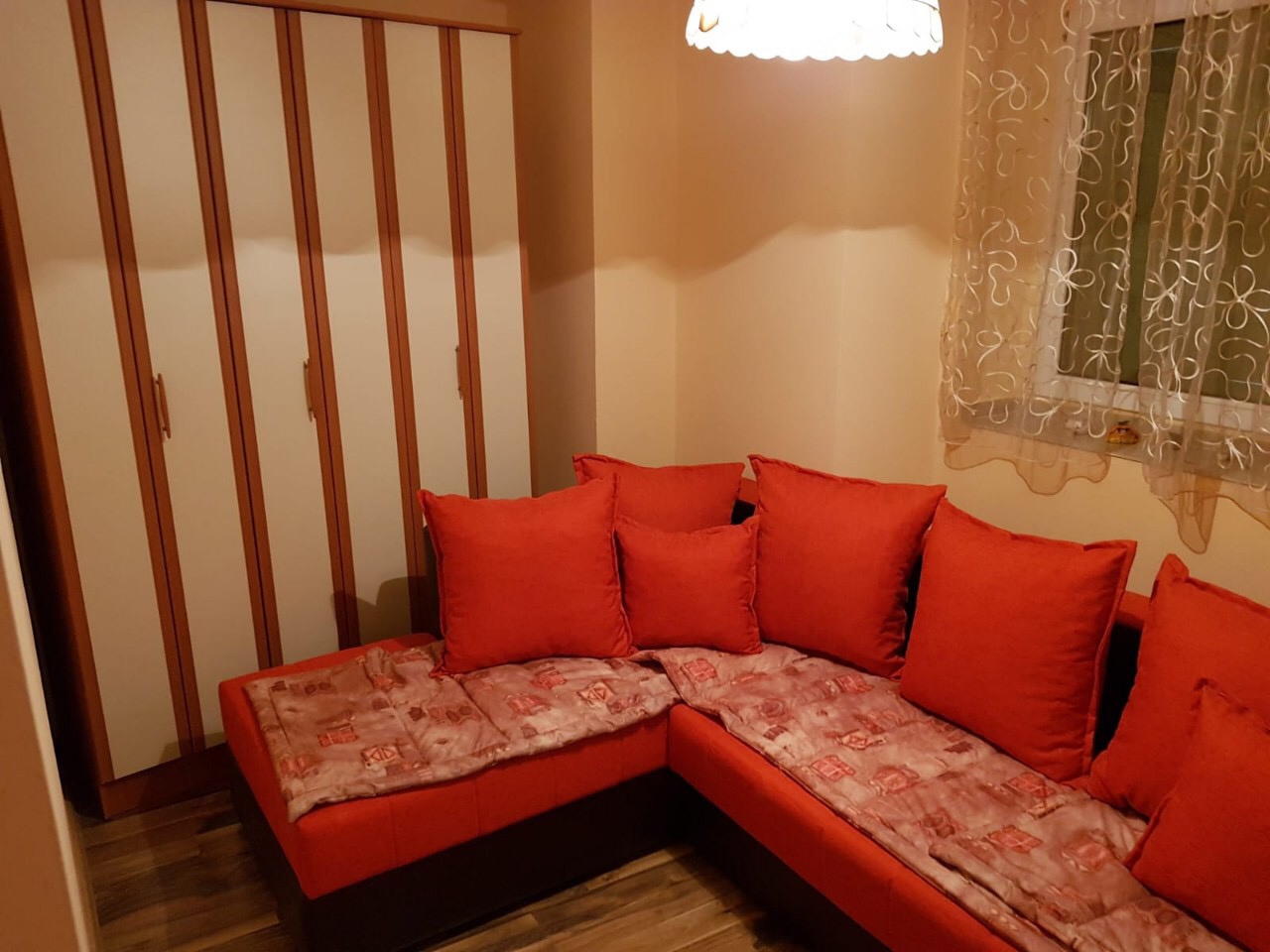 Gemütliches Wohnzimmer mit rotem Ecksofa und Schrank in einer Wohnung in Budva, Montenegro. Innenraum mit Parkettboden.