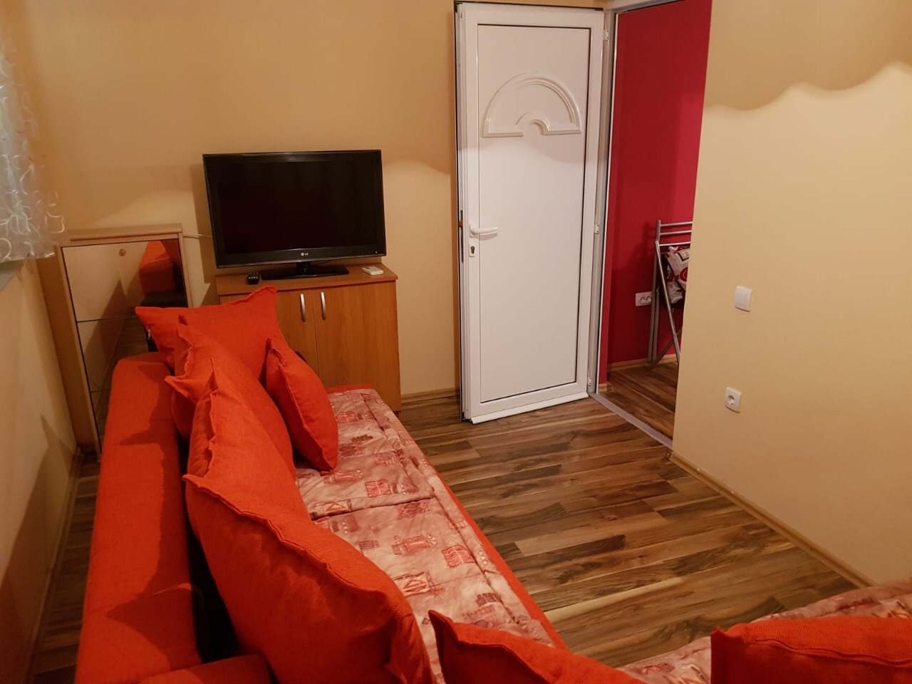 Wohnzimmer mit rotem Sofa, Fernseher und Laminat in einer zum Verkauf stehenden Wohnung in Budva, Montenegro.