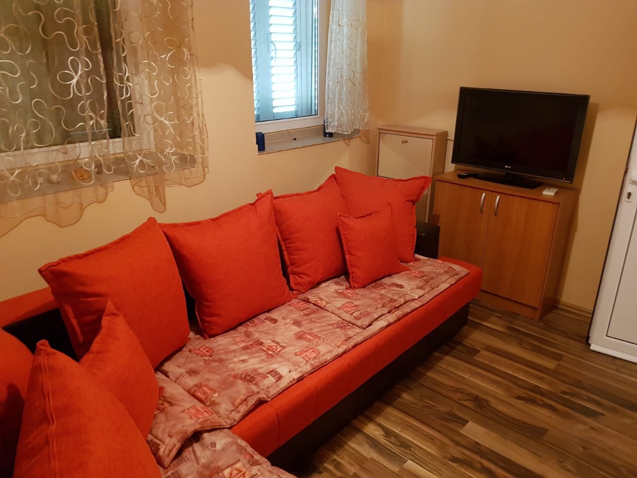 Gemütliches Wohnzimmer mit rotem Sofa und TV in einer zum Verkauf stehenden Wohnung in Budva, Montenegro. Innenraum mit Laminatboden und Fenster.