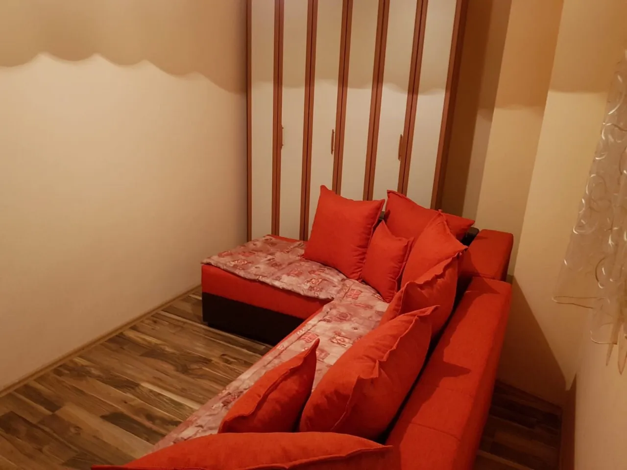 Kırmızı köşe koltuk ve gömme dolaplı уютlu oturma odası, Budva, Karadağ.