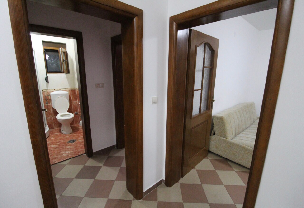 Flur im Haus an der Barer Riviera, Montenegro: Blick auf das Badezimmer mit Fliesen und auf den Raum mit Sofa und Holztüren.