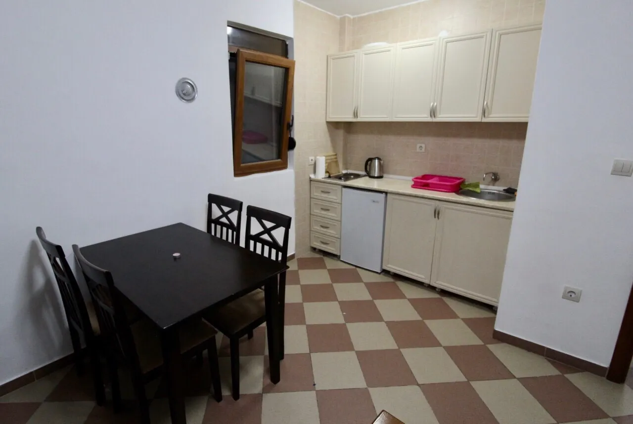 Une cuisine compacte avec des placards blancs, une petite table à manger avec des chaises et un sol carrelé.