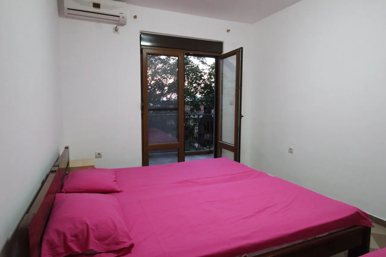 Chambre avec lit double, linge de lit rose et porte-fenêtre.
