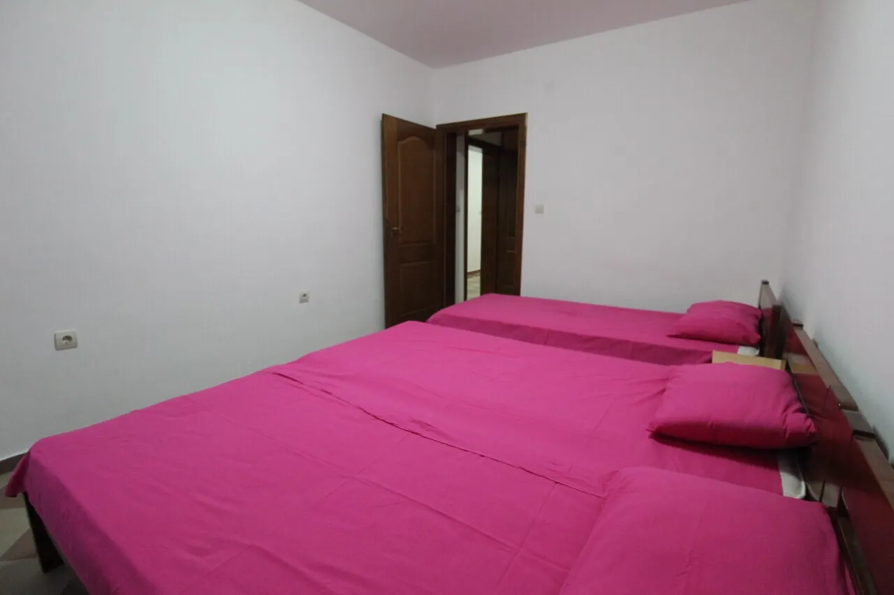 Une chambre avec trois lits roses, des murs blancs et des portes en bois ouvertes.