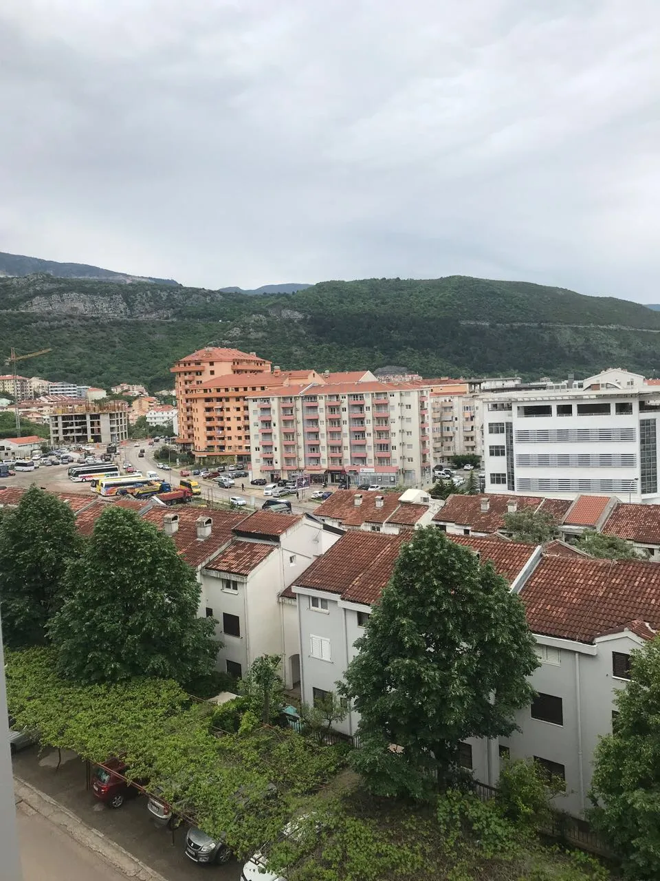 Panoramablick aus dem Fenster einer Wohnung in Budva, Montenegro: Stadtbebauung, Ziegeldächer und grüne Berge im Hintergrund.