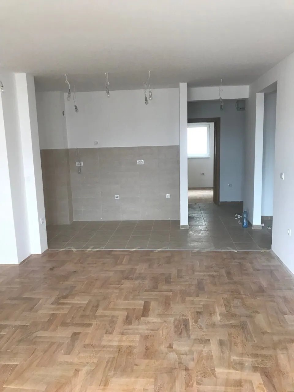 Küche mit Ausbau und Parkett in einer zum Verkauf stehenden Wohnung in Budva, Montenegro. Der Raum ist unmöbliert und verfügt über einen Kochbereich.