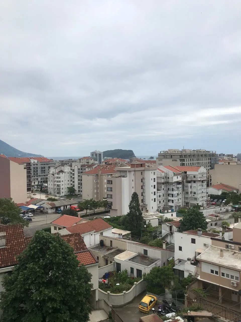 Panoramablick auf die Stadt Budva, Montenegro, mit Wohnhäusern, Ziegeldächern und der Meeresküste am Horizont.