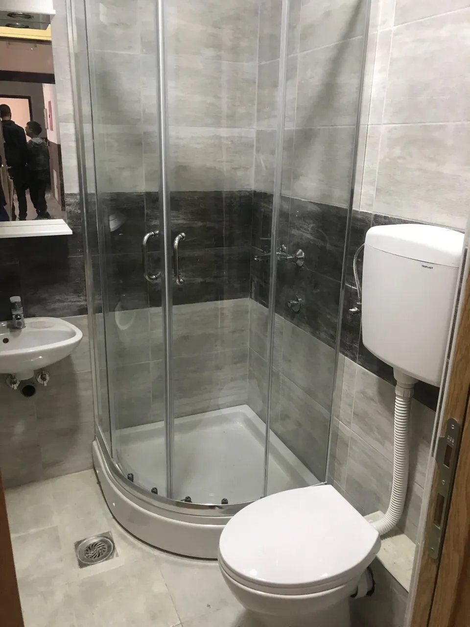 Modernes Badezimmer in einer Wohnung in Budva, Montenegro: Duschkabine, Waschbecken und WC in grauen Fliesen.