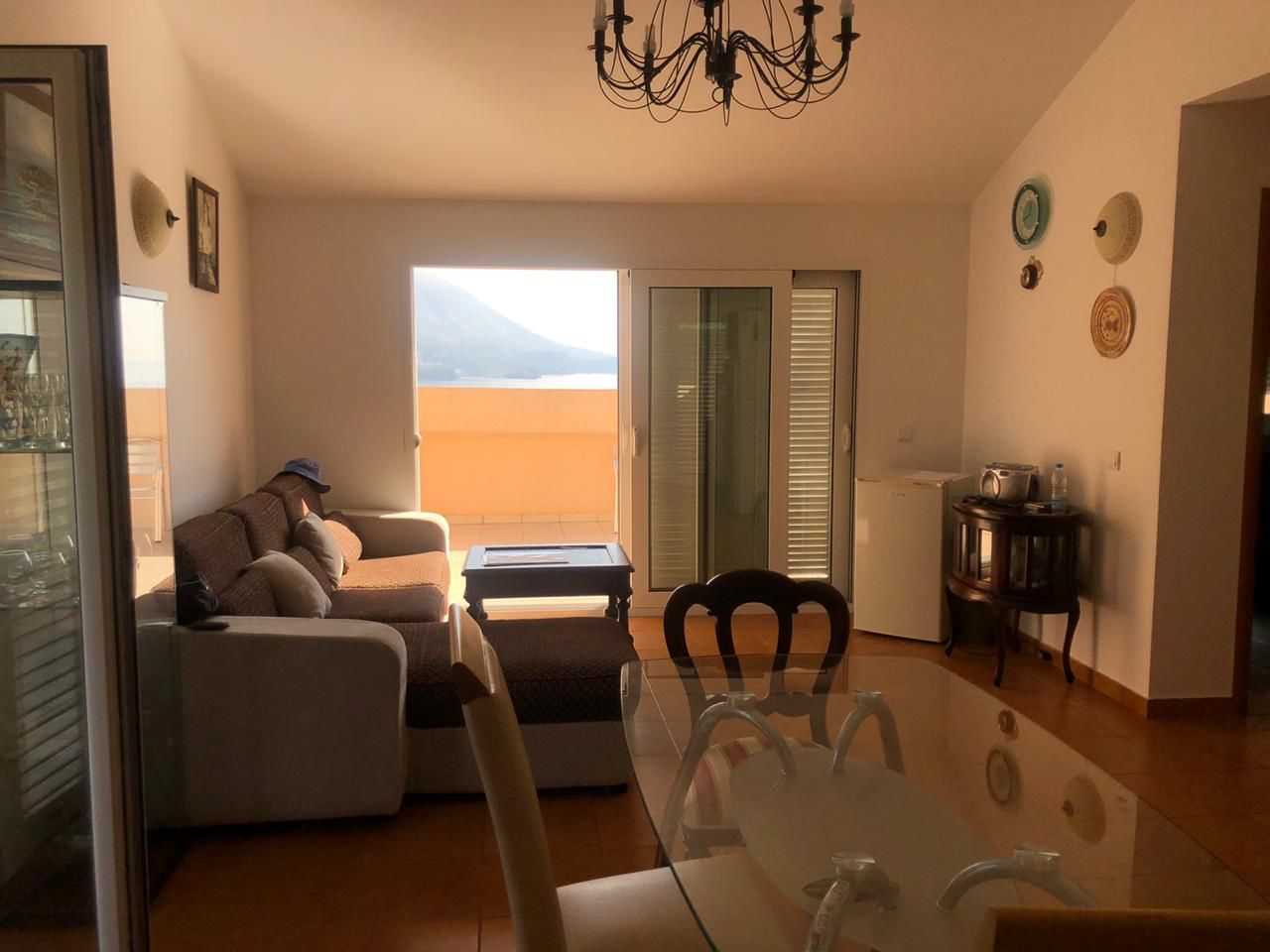 Wohnzimmer in einer Wohnung in Bečići, Montenegro: ein weiches Sofa, ein Glastisch und Zugang zur Terrasse mit Meerblick.
