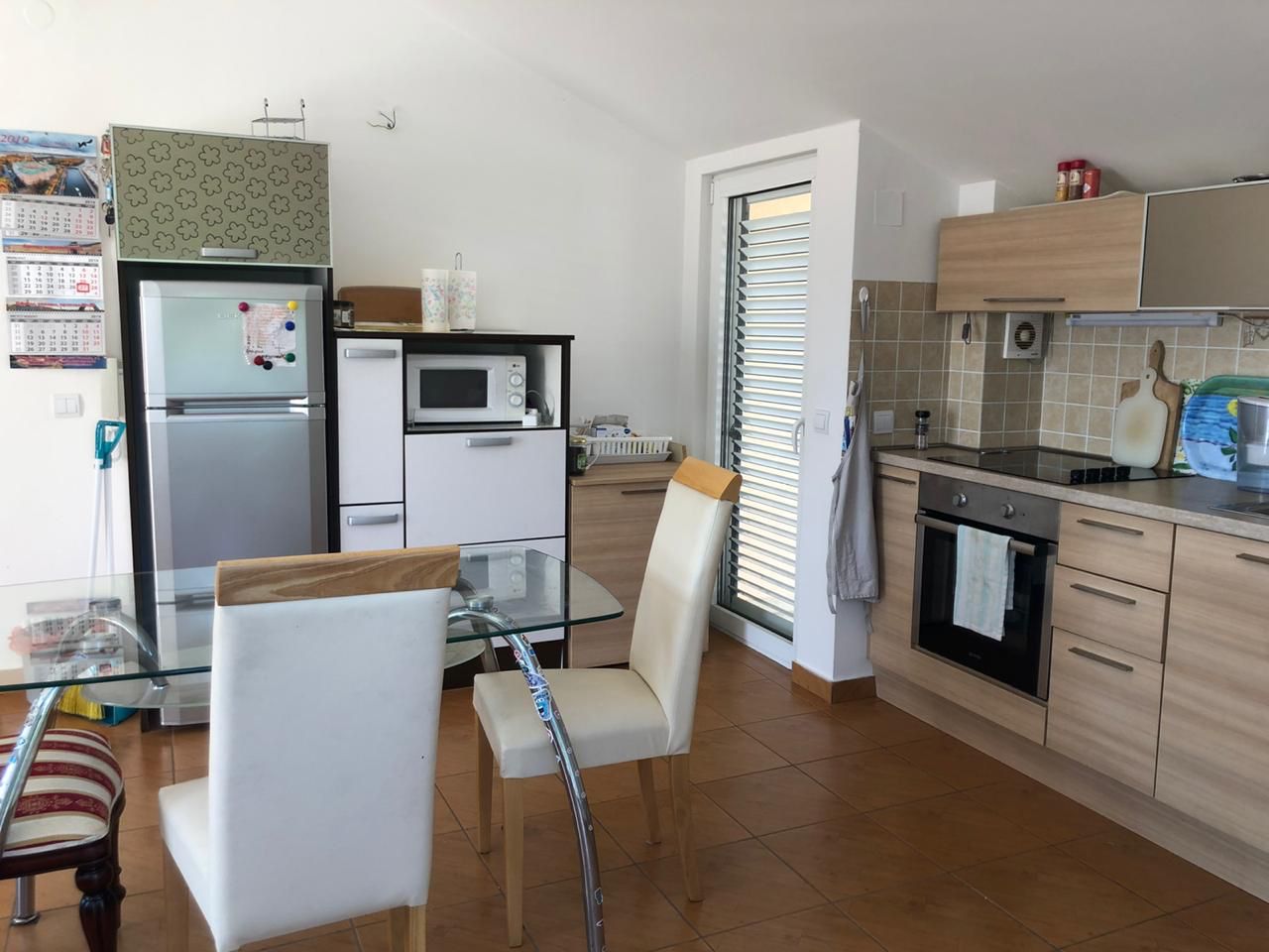 Helle Küche in einer Wohnung in Bečići, Montenegro: moderne Einbauküche, Essbereich mit Glastisch und Fliesen.