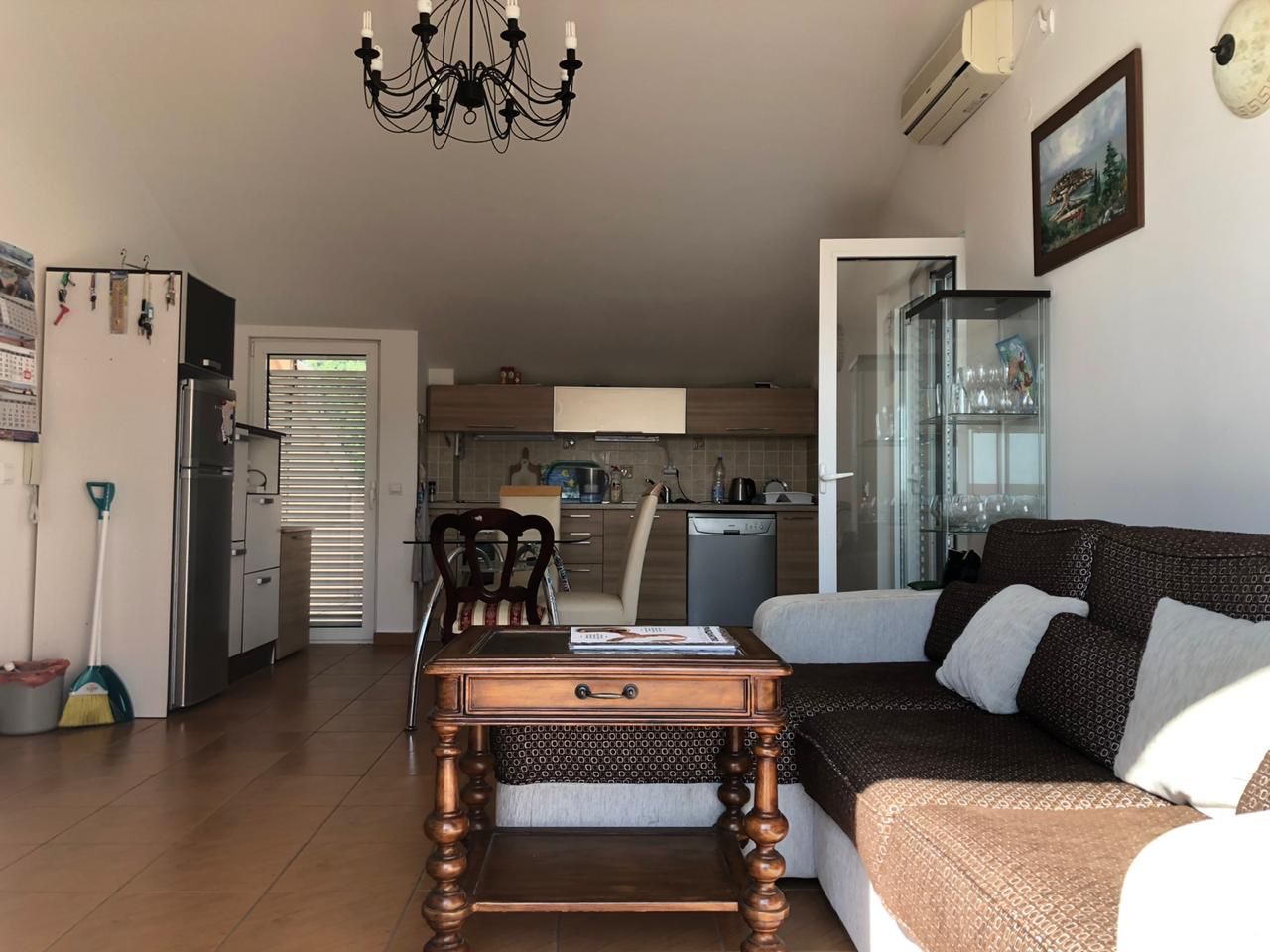 Wohnzimmer mit Küche in einer Wohnung in Bečići, Montenegro: ein weiches Sofa, ein Holztisch und eine Küchenzeile mit Geräten.