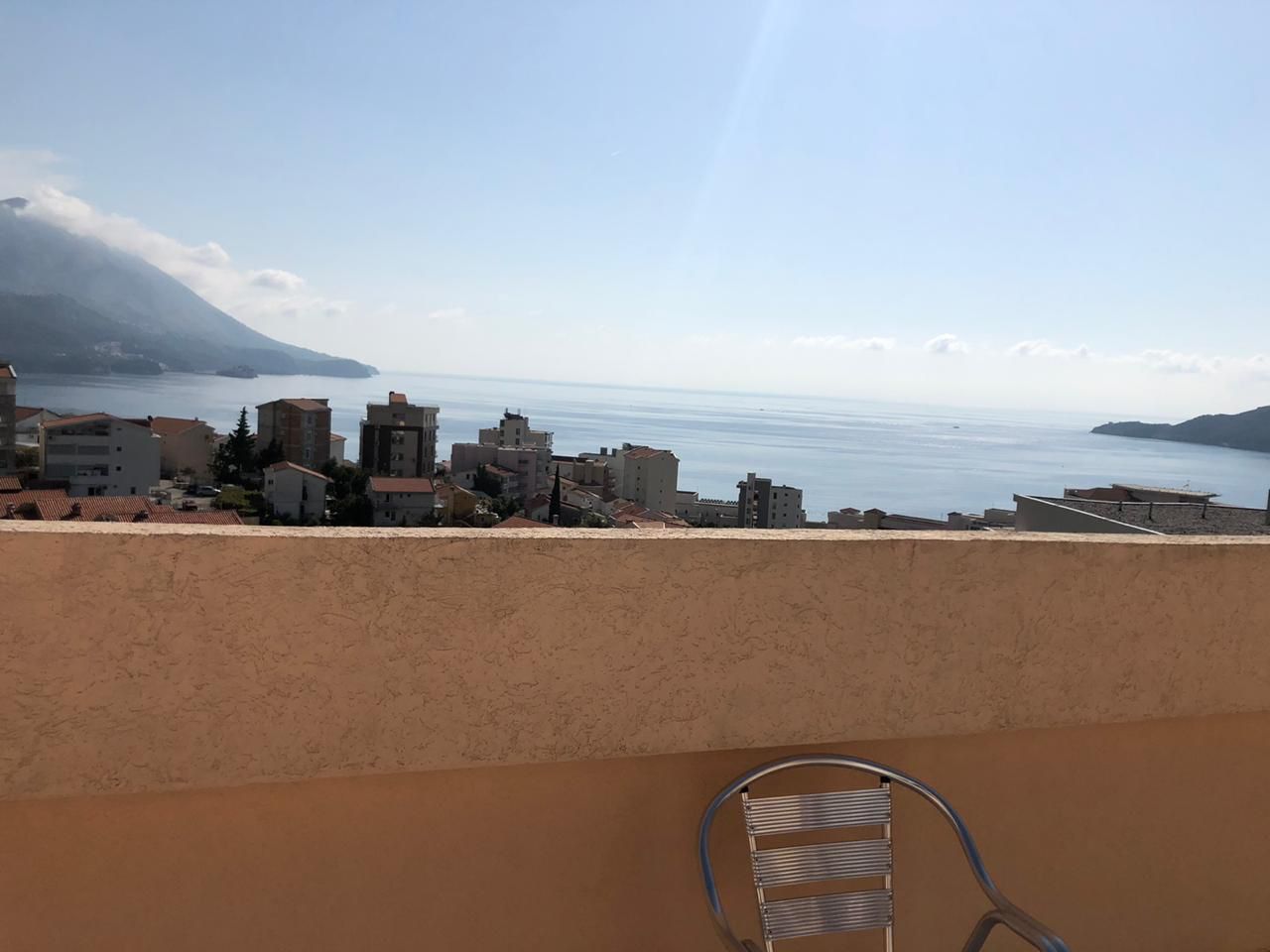 Blick auf das Meer und die Berge vom Balkon der Wohnung in Bečići, Montenegro: Panorama der Küste und metallische Gartenmöbel.