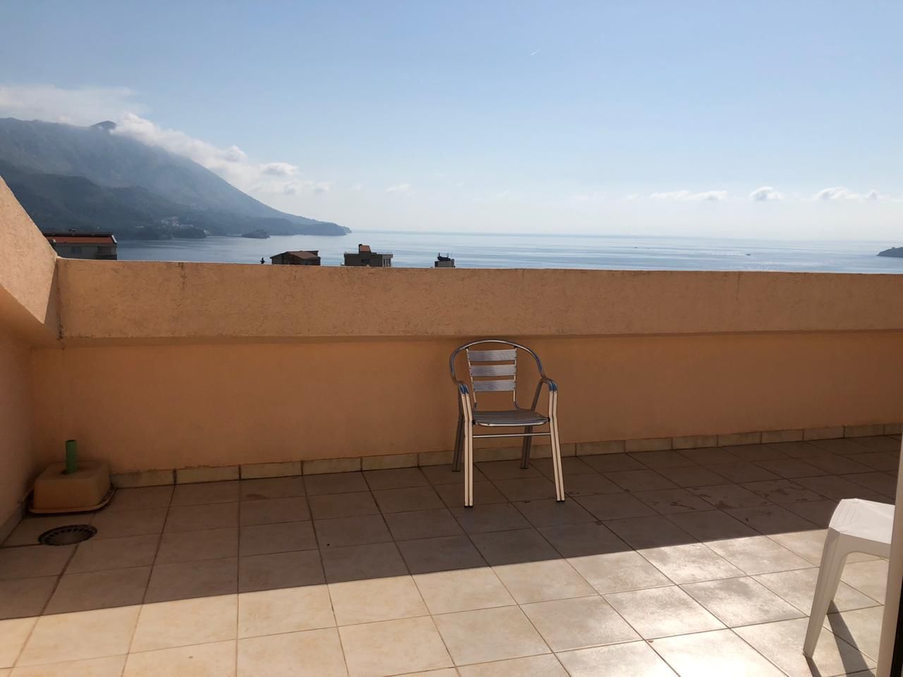 Terrasse der Wohnung in Bečići, Montenegro: Meer- und Bergblick, Fliesenboden, Metallstuhl, offener Balkon.