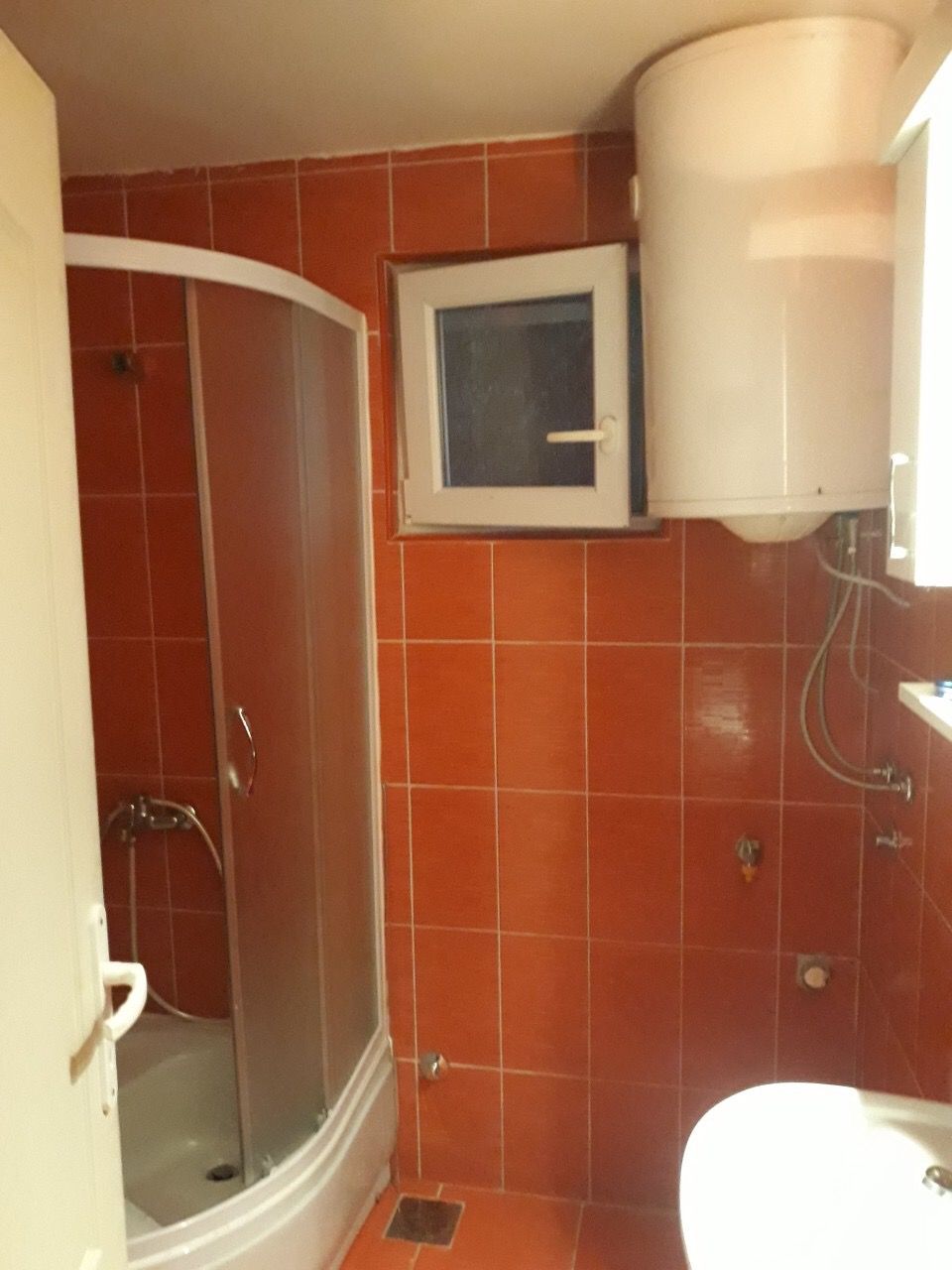 Łazienka z pomarańczowymi płytkami, kabiną prysznicową i bojlerem w domu na sprzedaż, Žanjica, Czarnogóra.