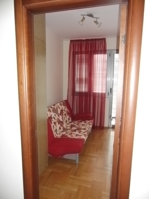 Wohnzimmer mit Sofa, Parkettboden und roten Vorhängen in einer Wohnung in Budva, Montenegro.