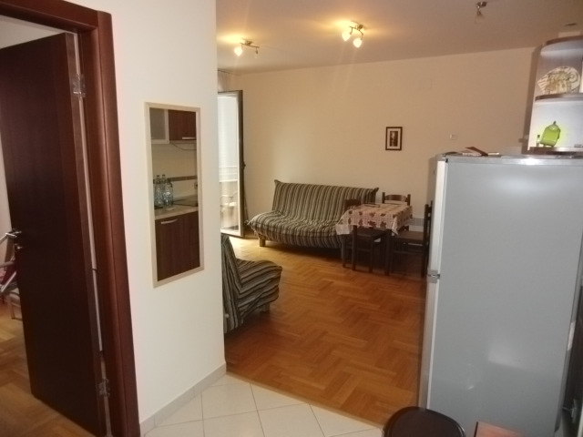 Wohnzimmer mit Parkett, Sofa und Essbereich in einer Wohnung in Budva, Montenegro. Blick auf die Küche und Ausgang zum Balkon.