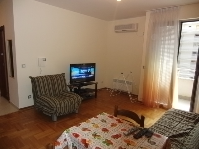 Wohnzimmer in einer Wohnung in Budva, Montenegro: Parkett, gestreifte Sessel, Esstisch, TV und Zugang zum Balkon.