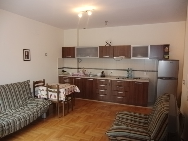 Küche mit Wohnzimmer, dunkler Einbauküche, Esstisch und Sofas in einer zum Verkauf stehenden Wohnung in Budva, Montenegro.