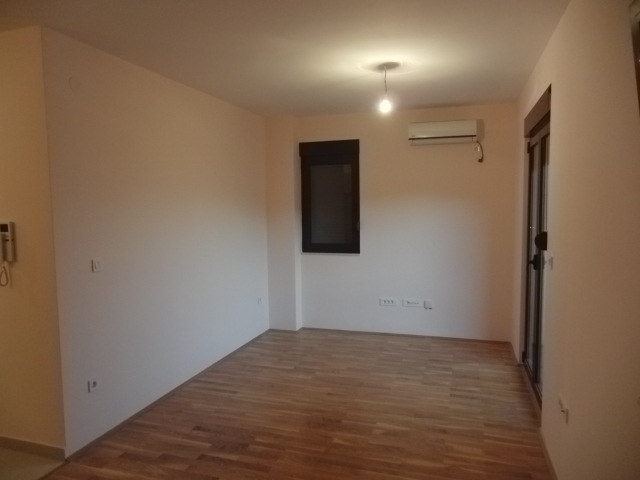 Helles Wohnzimmer mit Laminat, Klimaanlage und Zugang zum Balkon in einer zum Verkauf stehenden Wohnung in Budva, Montenegro.