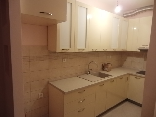 Helle Eckküche in einer Wohnung in Budva, Montenegro: beigefarbene Einbauküche, integrierte Spüle und Fliesen als Spritzschutz.
