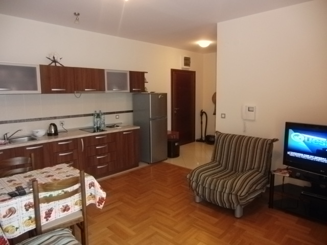 Wohnzimmer mit Küche in einer Wohnung in Budva, Montenegro: Holz-Einbauküche, Parkett, Esstisch und Sessel.