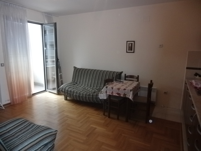 Wohnzimmer in einer Wohnung in Budva, Montenegro: gestreiftes Sofa, Esstisch, Parkettboden und Zugang zum Balkon.