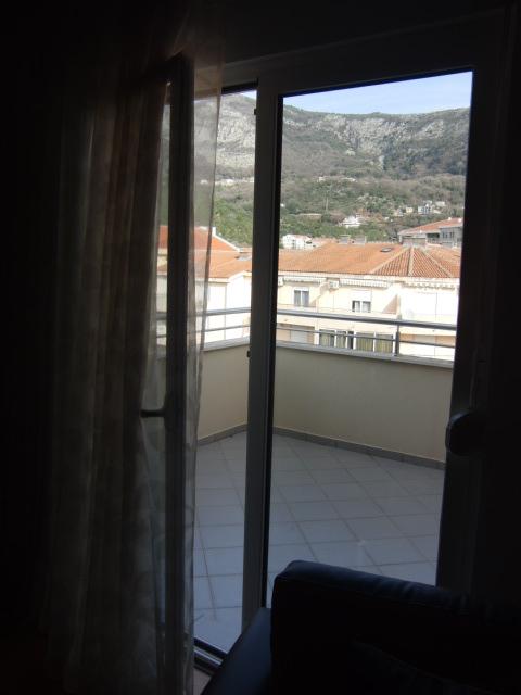 Blick vom Balkon der Wohnung in Budva, Montenegro: Panorama von Bergen und Ziegeldächern, Fliesenbelag, Ausgang aus dem Zimmer.