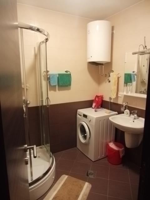 Badezimmer in einer Wohnung in Budva, Montenegro: Duschkabine, Waschmaschine, Boiler und Waschbecken mit Spiegel.