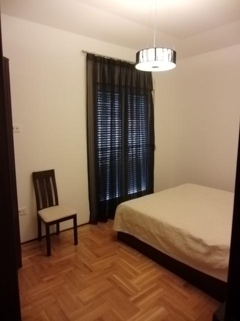 Helles Schlafzimmer mit Doppelbett und Holzstuhl in einer Wohnung, Budva, Montenegro. Parkettboden und Fenster mit Jalousien.